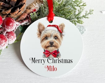 Puede incluir: Adorno navideño redondo blanco con un Yorkshire Terrier con gorro de Papá Noel y pajarita roja. El texto "Merry Christmas Milo" está impreso en escritura negra. Se adjunta una cinta roja para colgar.