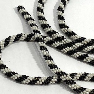 May include: A close-up of a black and white beaded cord. The cord is made of small, round beads that are arranged in a spiral pattern. The cord is thick and durable, and it would be perfect for making jewelry or other crafts.