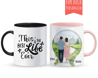 May include: Two personalized coffee mugs with black and pink rims. One mug features the text "This is the best life ever" in black lettering. The other mug features a watercolor illustration of a couple walking in a mountain landscape with the names "Paul" and "Denise" written below.