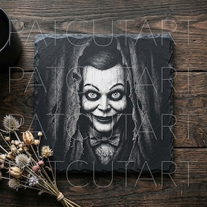 May include: A square black slate coaster featuring a white engraved illustration of a ventriloquist dummy with wide eyes, a prominent smile, and a bowtie, surrounded by a draped fabric texture, with the text PATCUTART overlaid on the image.