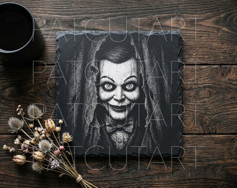 May include: A square black slate coaster featuring a white engraved illustration of a ventriloquist dummy with wide eyes, a prominent smile, and a bowtie, surrounded by a draped fabric texture, with the text PATCUTART overlaid on the image.