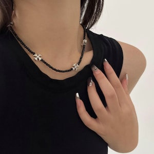 May include: A black beaded necklace with silver cross pendants. The necklace is worn against a black top. The silver crosses are evenly spaced along the necklace. The necklace is a stylish accessory.