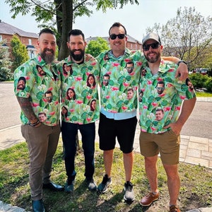 May include: Four friends wearing green and white tropical print shirts with different faces printed on them. The shirts have pink flamingos and green leaves. The friends are standing outside in front of a building.