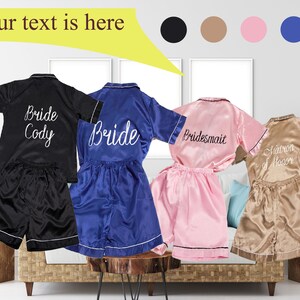May include: Four satin pajama sets in black, blue, pink, and beige with embroidered text. The black set says "Bride Cody", the blue set says "Bride", the pink set says "Bridesmaid", and the beige set says "Matron of Honor".