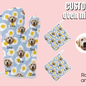 May include: Custom oven mitts and pot holders featuring a light blue background with a pattern of fried eggs and a golden retriever's face. The name "Zeus" is printed on the mitts. The set includes an oven mitt and two pot holders.