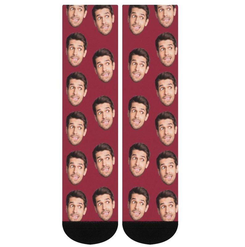 K&ouml;nnte beinhalten: Ein Paar rote Socken mit einem sich wiederholenden Muster eines M&auml;nnergesichts. Die Socken haben schwarze B&uuml;ndchen.