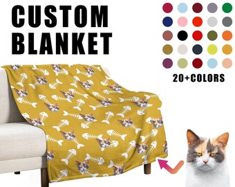 May include: A custom blanket with a yellow background and a repeating pattern of white fish bones and a cat's face. The text "CUSTOM BLANKET" is at the top of the image. A color chart with 20+ colors is shown on the right side of the image. The text "20+ COLORS" is below the color chart.