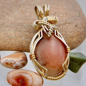 May include: A pendant featuring a pink and white agate stone wrapped in silver and gold wire.