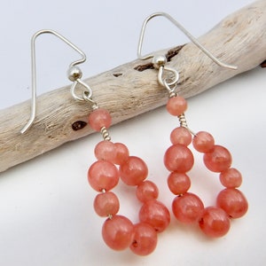 May include: A pair of dangle earrings with a teardrop shape made of pink beads and silver hooks.