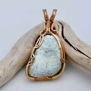 May include: A gold wire wrapped pendant featuring a light gray and white speckled stone.