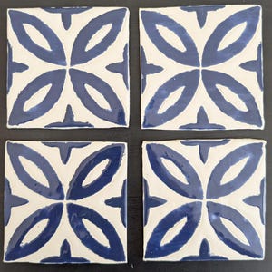 May include: Four square ceramic tiles with a white background and a blue floral design. Each tile features a four-petal flower pattern in a glossy blue glaze. The tiles are arranged in a square formation.