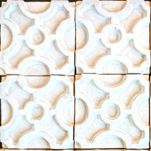 May include: A set of four square off-white ceramic tiles arranged in a grid. Each tile features a raised, symmetrical geometric pattern consisting of interconnected circles and curved lines, creating a repeating lattice design across the surface.