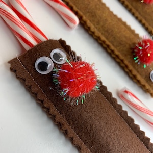 Könnte beinhalten: Ein braunes Filz-Rentier-Ornament mit einem Zuckerstangen-Innenteil. Das Rentier hat Glitz Augen, eine rote Pompon-Nase und glitzernden roten Glitzer.