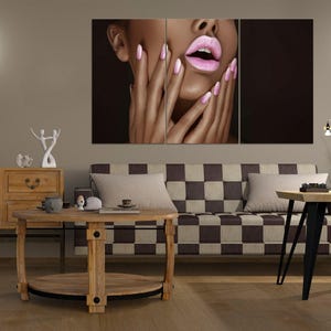 Può includere: Una stampa artistica su tela a tre pannelli con un primo piano del viso di una persona con rossetto rosa e unghie lunghe e rosa. L'opera d'arte è esposta sopra un soggiorno con un divano a scacchi e mobili in legno.