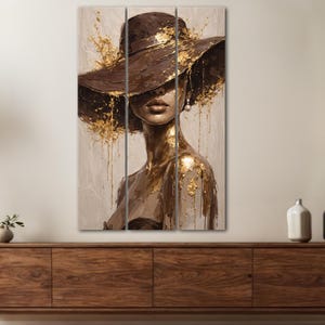 May include: A triptych canvas print featuring a woman in a wide-brimmed brown hat. The artwork has gold accents and a neutral background. The woman's face is partially obscured, and the overall style is artistic and elegant.