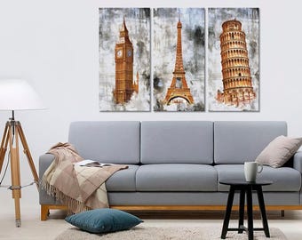 May include: A triptych canvas art print featuring iconic landmarks: Big Ben, the Eiffel Tower, and the Leaning Tower of Pisa. The artwork has a watercolor effect with brown and gray tones. The art is displayed above a gray sofa.