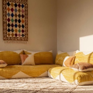 May include: A low-profile sectional sofa featuring a textured mustard yellow and cream geometric pattern. The sofa is accented with several small square throw pillows in shades of burnt orange and brown, arranged on the seat cushions.