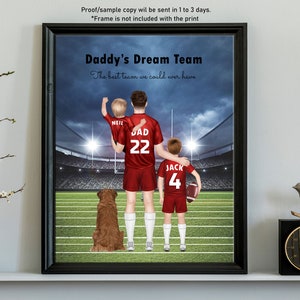 Pode incluir: Uma impress&atilde;o emoldurada de um pai e dois filhos com camisas de futebol vermelhas em p&eacute; em um campo de futebol. O pai est&aacute; segurando seu filho mais novo em seus ombros. A impress&atilde;o tem o texto "Daddy's Dream Team" e "The best team we could ever have".