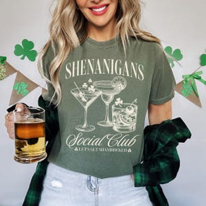 May include: A green t-shirt with the text "Shenanigans Social Club Let's Get Shamrocked" and a graphic of three cocktail glasses.
