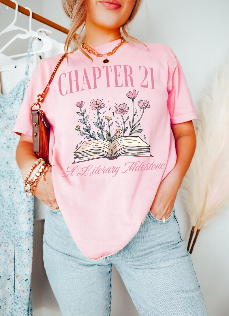 May include: Pink t-shirt with the text "Chapter 21 A Literary Milestone" and a graphic of an open book with flowers growing from it.