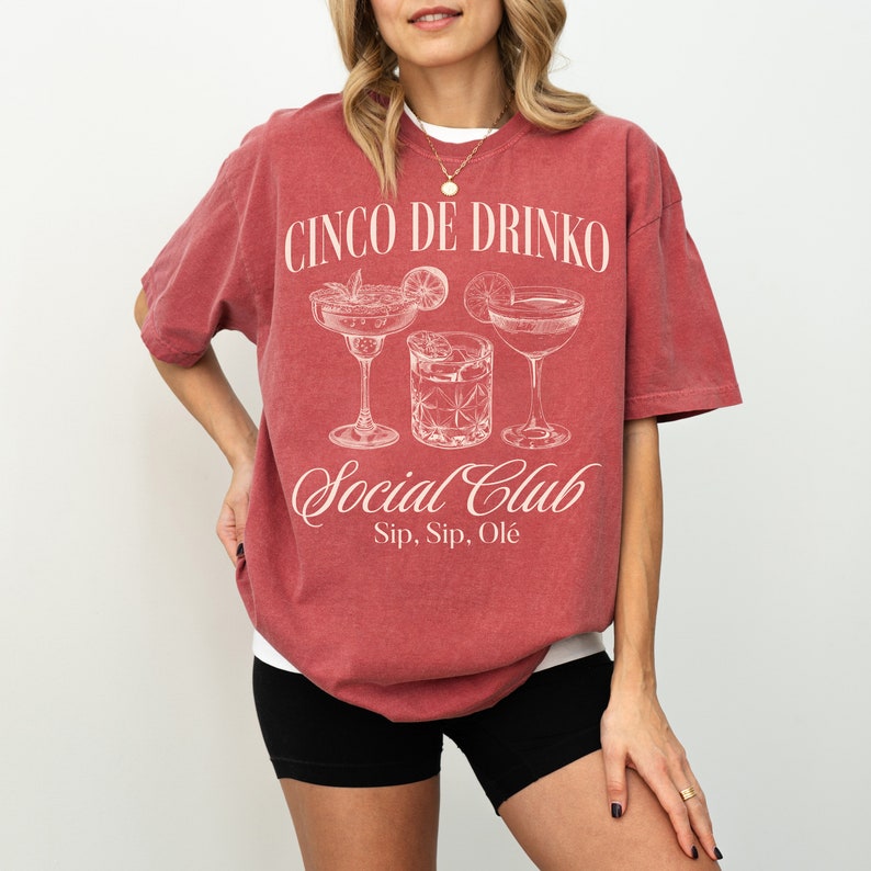 May include: A red t-shirt with the text "Cinco de Drinko Social Club Sip, Sip, Ol&egrave;" and a graphic of three cocktail glasses.