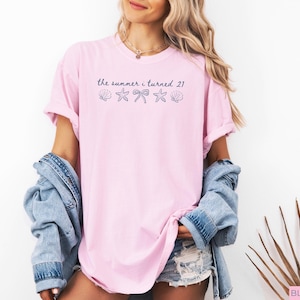 Pu&ograve; includere: T-shirt rosa chiaro con la scritta "the summer i turned 21" e grafiche di conchiglie, fiocco e stella marina. La maglietta &egrave; di vestibilit&agrave; ampia.