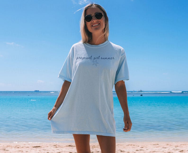 May include: A light blue t-shirt with the text "pregnant girl summer" in purple lettering and a small starfish graphic.