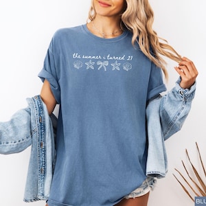 Pu&ograve; includere: Una maglietta blu jeans con la scritta "the summer i turned 21" e grafiche di conchiglie, stelle marine e fiocchi. La maglietta ha una vestibilit&agrave; ampia e maniche arrotolate. Una giacca di jeans &egrave; drappeggiata sulle spalle.
