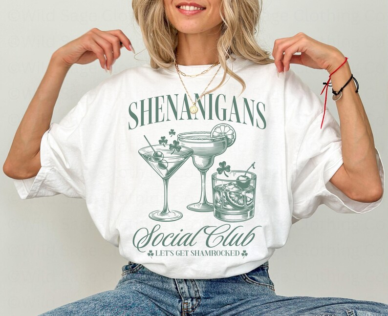 May include: White t-shirt with a green graphic design that says "Shenanigans Social Club" and features three cocktail glasses with shamrock accents. The text below the glasses says "Let's Get Shamrocked."
