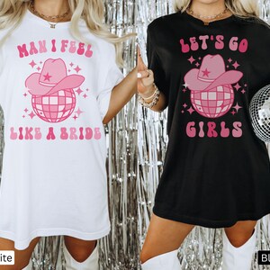 K&ouml;nnte beinhalten: Zwei wei&szlig;e und schwarze T-Shirts mit einem pinkfarbenen Disco-Ball und einem Cowboyhut-Motiv. Das wei&szlig;e Shirt sagt "Man I feel like a bride" und das schwarze Shirt sagt "Let's go girls".