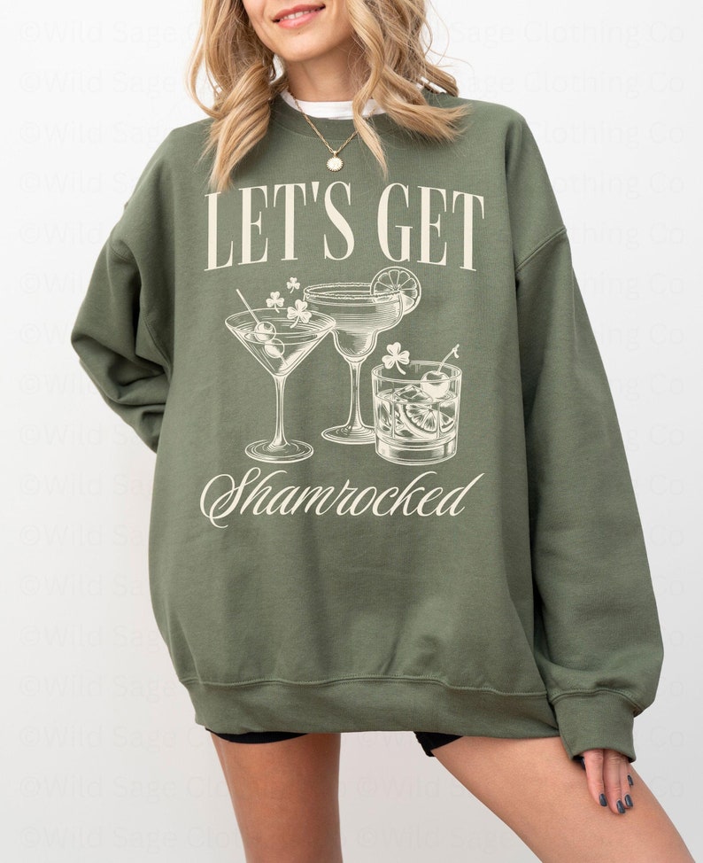 以下が含まれることがあります： 「Let's Get Shamrocked」という文字と、3つのカクテルグラスのグラフィックが描かれた緑色のスウェットシャツです。