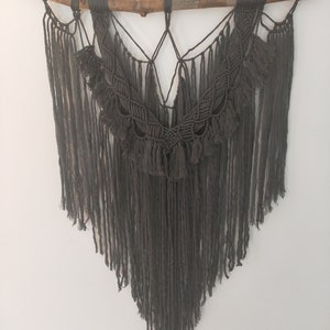 May include: A gray macrame wall hanging with a wooden branch at the top and a fringe design.