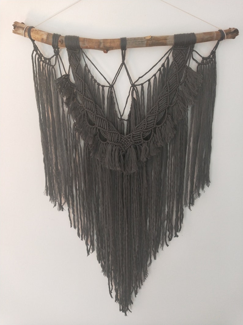 May include: A gray macrame wall hanging with a wooden branch at the top and a fringe design.