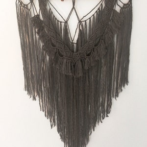 May include: A gray macrame wall hanging with a wooden branch at the top and long fringe tassels.