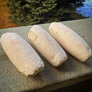 May include: Three white chalk sticks, each with a slightly different shape and texture, are arranged on a grey surface. The chalk sticks are all slightly rounded and have a rough, textured surface.
