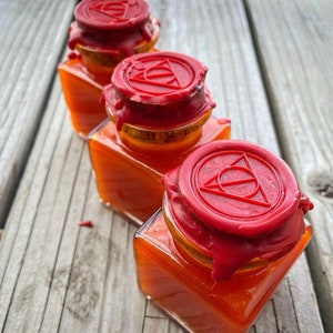 May include: Three small glass jars with orange liquid inside. Each jar has a red wax seal on the lid with a triangle symbol.