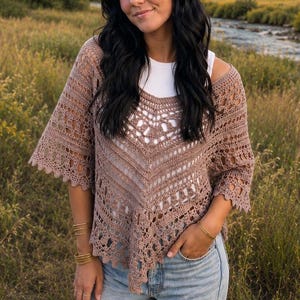 May include: A mauve crochet top featuring an intricate openwork pattern with a V-neckline and wide, elbow-length sleeves, worn over a plain white tank top paired with light blue distressed denim jeans with rips at the knees.