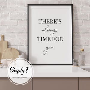 Puede incluir: Una impresi&oacute;n enmarcada con el texto "THERE'S always TIME FOR gin" en escritura negra. La impresi&oacute;n est&aacute; en un marco negro y se muestra en una encimera blanca. El fondo presenta una pared de ladrillos blancos.