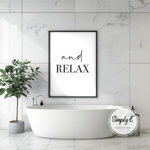 Puede incluir: Una impresi&oacute;n enmarcada en negro con las palabras "and RELAX" en un entorno de ba&ntilde;o. Una ba&ntilde;era blanca est&aacute; en primer plano, con una planta en maceta a la izquierda. El fondo presenta baldosas de m&aacute;rmol blanco.