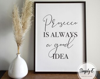 May include: Black and white printable wall art with the text "Prosecco is always a good idea". The print is framed in a black frame and is sitting on a wooden surface.