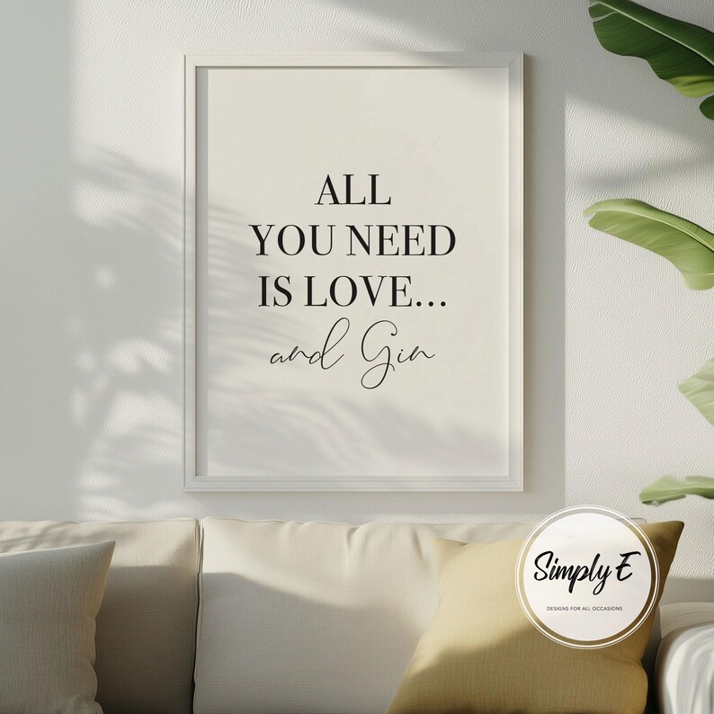 Peut inclure: Une affiche encadr&eacute;e avec le texte "ALL YOU NEED IS LOVE... and Gin" en script noir. L'affiche est dans un cadre blanc et est accroch&eacute;e au-dessus d'un canap&eacute; cr&egrave;me avec un coussin jaune. L'image est dans une pi&egrave;ce bien &eacute;clair&eacute;e avec une plante en arri&egrave;re-plan.