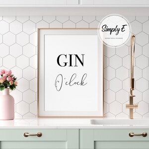 Puede incluir: Un cartel enmarcado con las palabras "GIN O'clock" en escritura negra. El cartel est&aacute; en un marco dorado y se exhibe en un entorno de cocina. Tambi&eacute;n se ve un jarr&oacute;n rosa con flores y un grifo dorado.