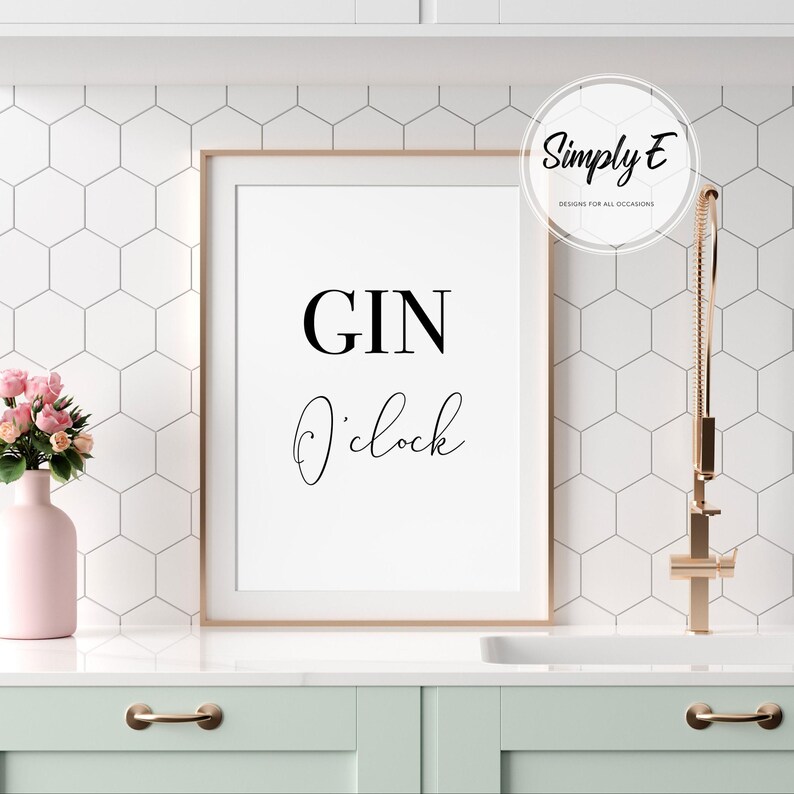 Puede incluir: Un cartel enmarcado con las palabras "GIN O'clock" en escritura negra. El cartel est&aacute; en un marco dorado y se exhibe en un entorno de cocina. Tambi&eacute;n se ve un jarr&oacute;n rosa con flores y un grifo dorado.
