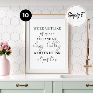 May include: A rectangular wall art print in a thin copper frame featuring black text on a white background that reads: WE'RE A BIT LIKE prosecco YOU AND ME, classy, bubbly & OFTEN DRUNK at parties. The print is displayed in a kitchen setting.