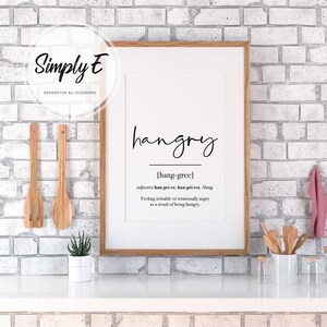 K&ouml;nnte beinhalten: Ein wei&szlig;er gerahmter Druck mit dem Wort "hangry" in schwarzer Kursivschrift. Die Definition von hangry ist darunter in schwarzer Schrift geschrieben: "[hang-gree] Adjektiv han-gri-er, han-gri-est. Slang. Sich gereizt oder irrational w&uuml;tend f&uuml;hlen, weil man hungrig ist."