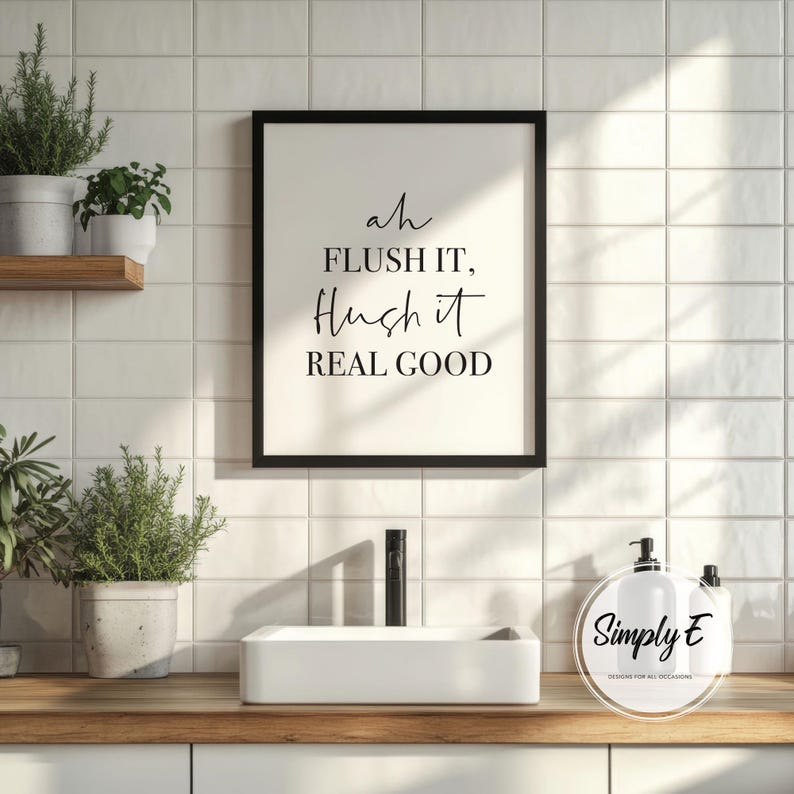 May include: A framed print with the text "ah FLUSH IT, Hush it REAL GOOD" in black font. The print is in a black frame and hangs on a white tiled wall. A white sink and plants are in the foreground.
