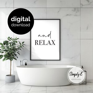 May include: A framed wall art print featuring the text and RELAX in black lettering on a white background. The artwork is displayed above a white freestanding bathtub in a bathroom with white marble-patterned wall and floor tiles.