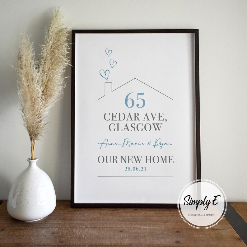 Peut inclure: Impression encadr&eacute;e avec un cadre noir. L'impression pr&eacute;sente une illustration de maison et du texte, dont l'adresse "65 Cedar Ave, Glasgow", les noms "Anne-Marie & Ryan" et "OUR NEW HOME 25.06.21". Un vase avec des plantes s&eacute;ch&eacute;es est &agrave; gauche.