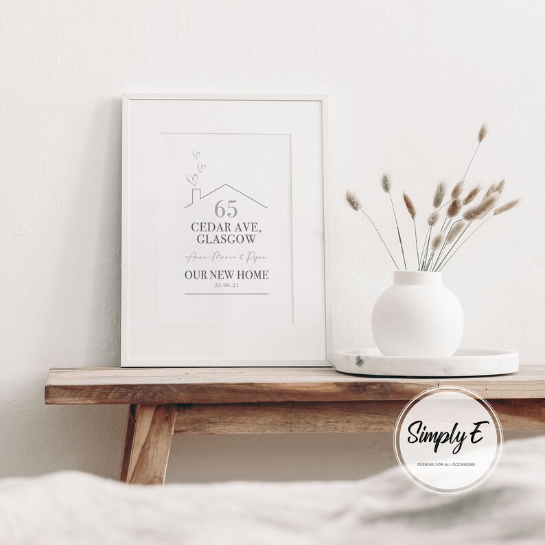 Peut inclure: Un cadre blanc avec l'inscription "65 Cedar Ave, Glasgow, Our New Home" dans un design minimaliste. Un vase blanc avec des fleurs s&eacute;ch&eacute;es est pos&eacute; sur un plateau en marbre &agrave; c&ocirc;t&eacute; du cadre.