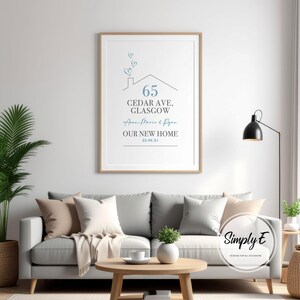 Peut inclure: Un cadre en bois clair encadre une affiche au-dessus d'un canap&eacute; gris. L'affiche pr&eacute;sente un dessin de maison avec le num&eacute;ro 65, une adresse, des noms et le texte &laquo;&nbsp;NOTRE NOUVELLE MAISON&nbsp;&raquo; dans un style minimaliste. L'affiche est dans un salon.